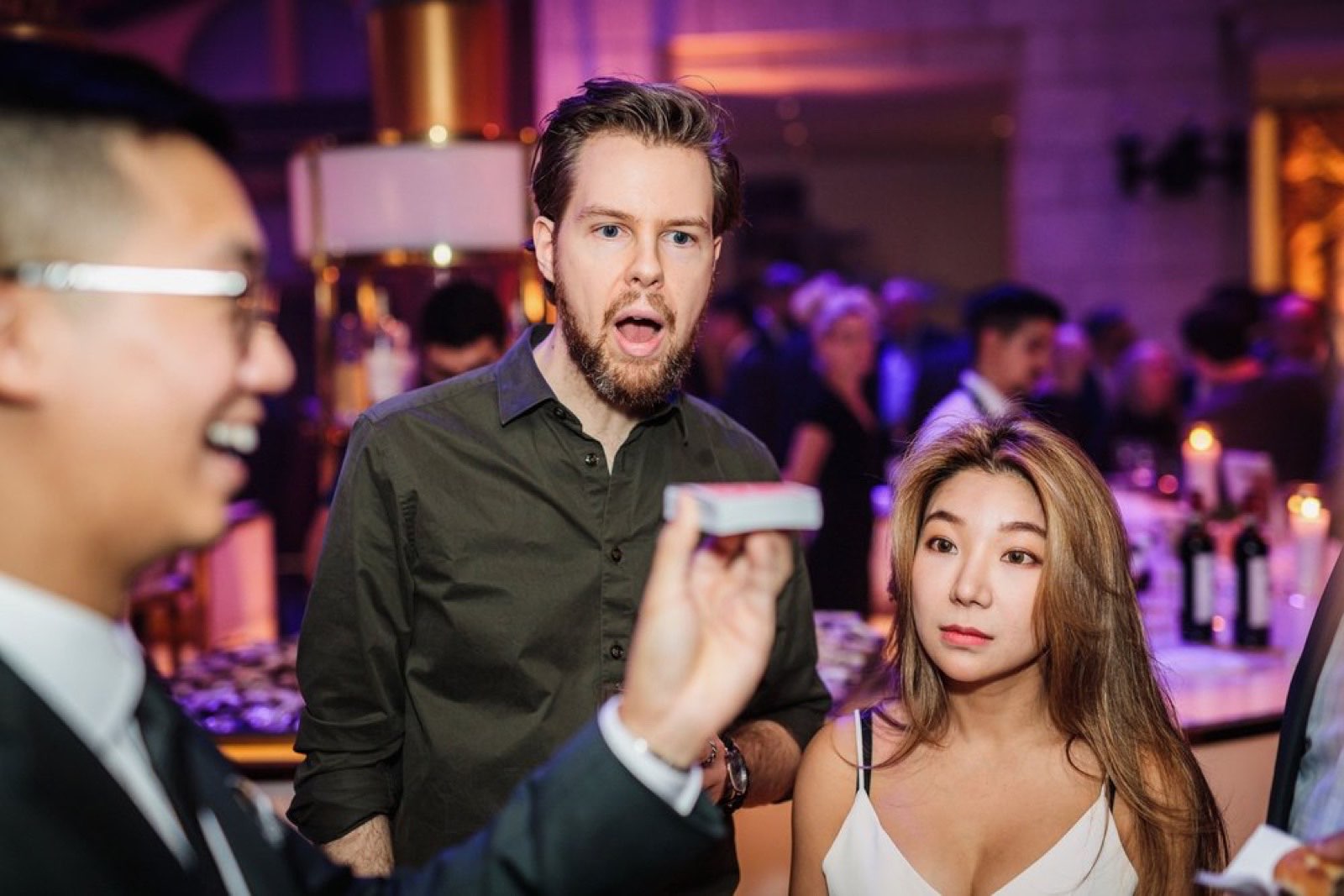 A guest reacts open-mouthed as Bao performs close-up magic at an upscale Montreal event